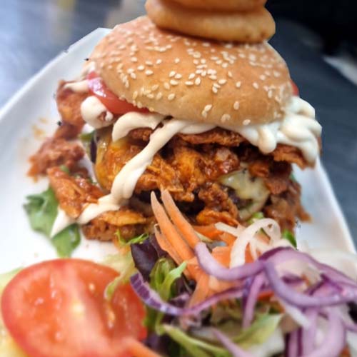 A towering stacked chicken burger with onion rings and salad